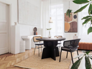 Stylish and modern dining room interior with design sharing table, chairs, gold pendant lamp, abstract paintings and elegant accessories. Tropical leafs in vase. Eclectic home decor. ; Shutterstock ID 1922829779; purchase_order: -; job: -; client: -; other: -